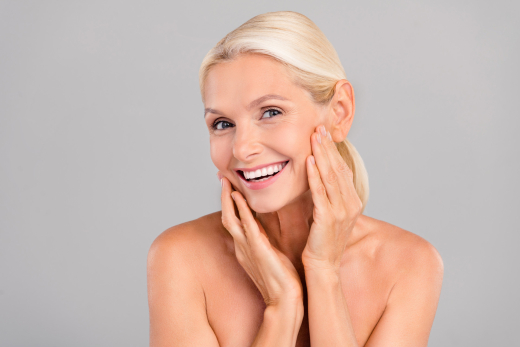A middle-aged woman with radiant, glowing skin smiles warmly, exuding confidence and beauty.