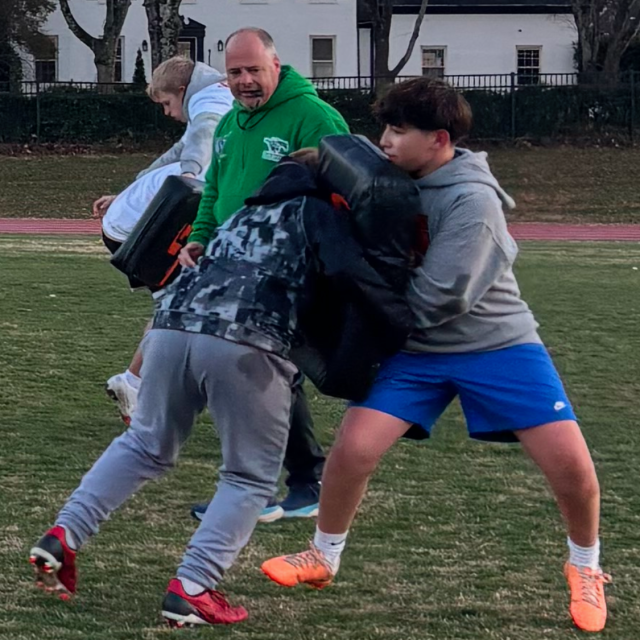 Dr. Cook coaching a youth rugby team on the field.