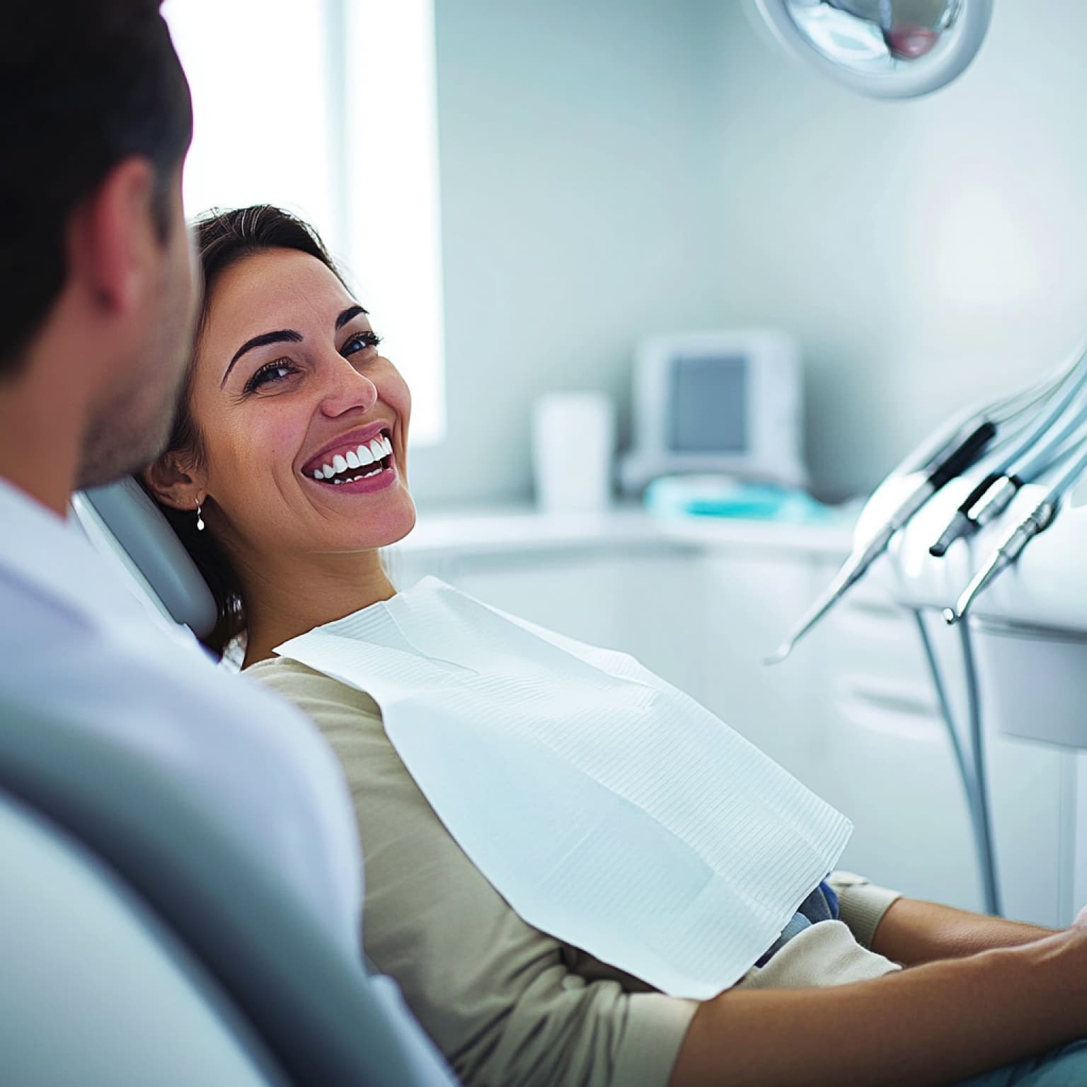 Two persons in a dental office, one smiling in a chair, with dental equipment visible in a clean, modern setting.