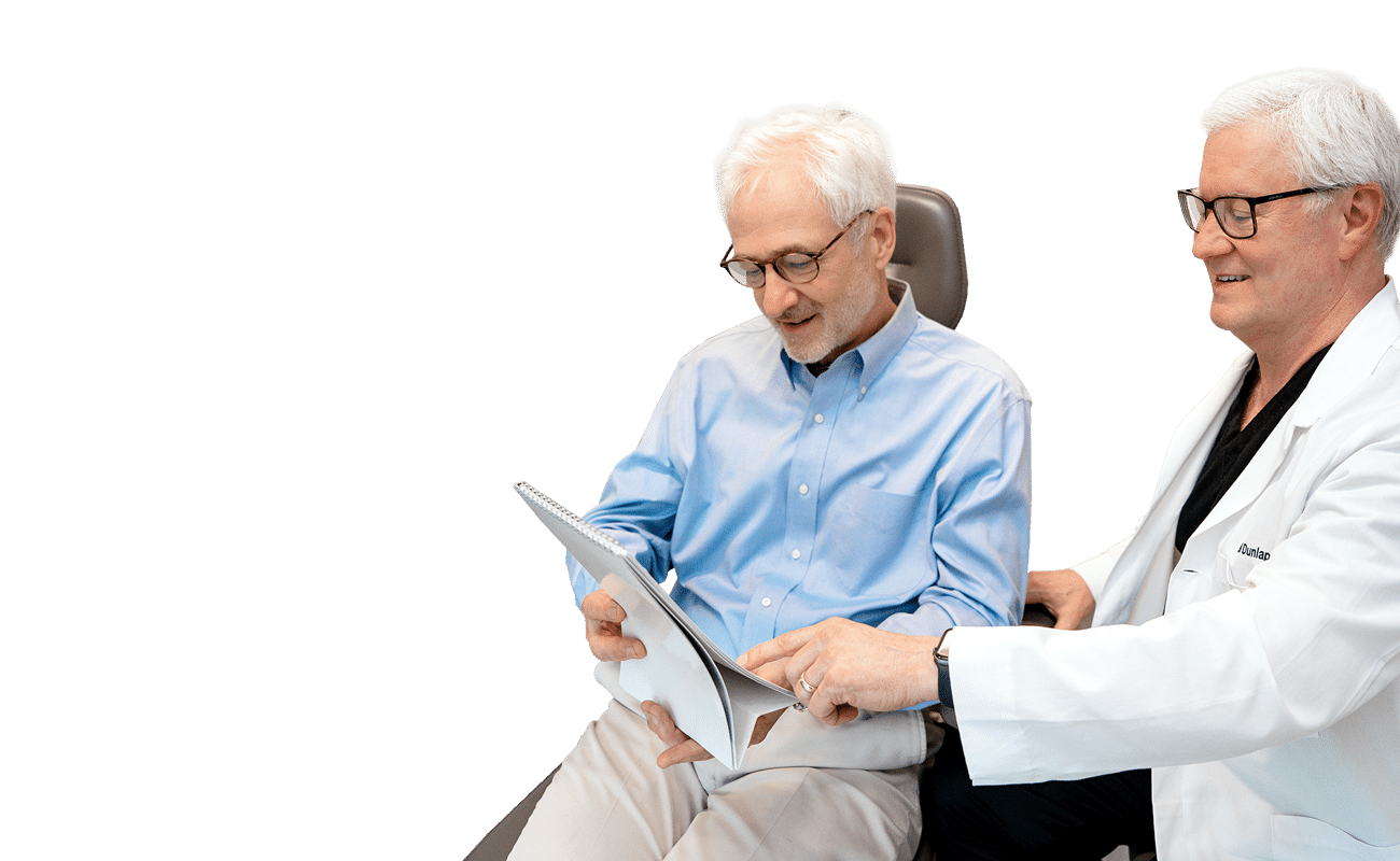 Two people in a medical office review documents together. One person wears a lab coat, indicating a professional healthcare setting.