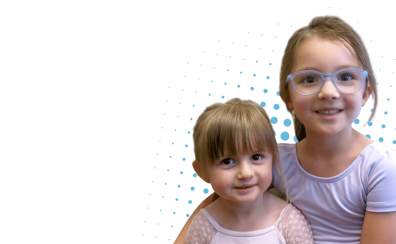 Smiling children with glasses, against a black background with blue dots. The older embraces the younger, both appearing happy and playful.
