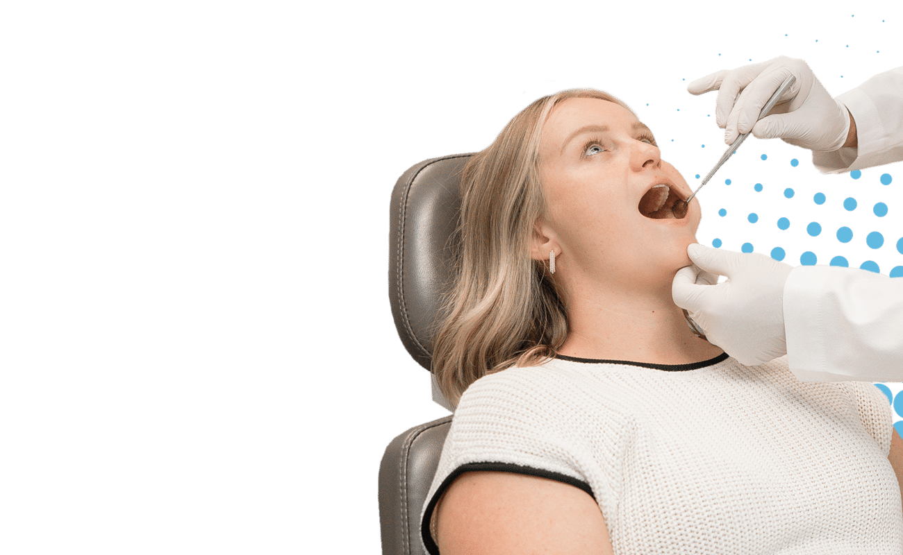 A person undergoes a dental examination. Gloved hands hold a tool for inspection. Background features a dotted pattern on a contrasting black surface.