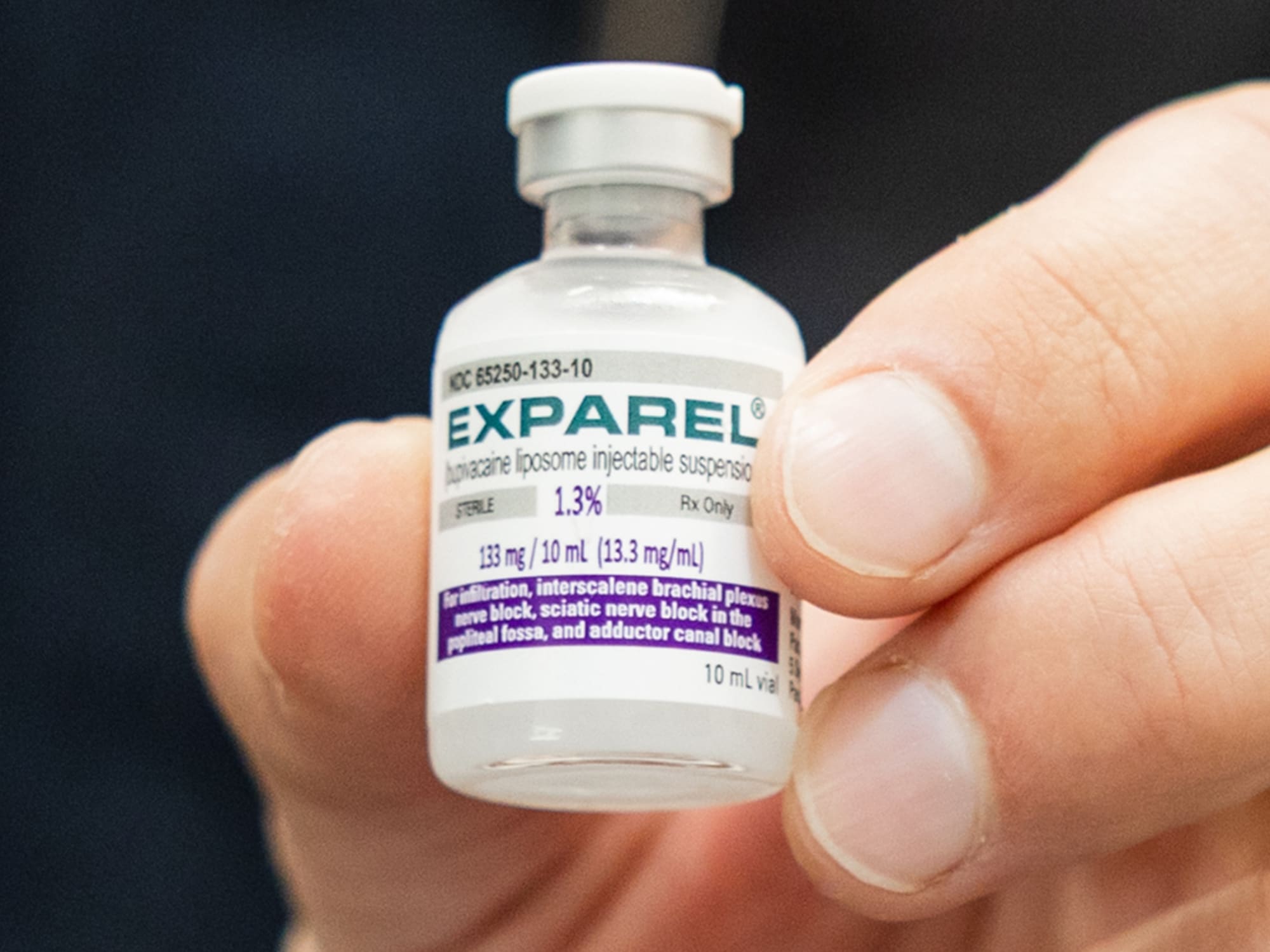 A person holds a vial of EXPAREL, a bupivacaine liposome injectable suspension, labeled with dosage and usage information, against a blurred background.