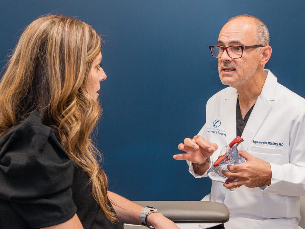 A person in a white coat explains to another person using a model against a plain blue background, suggesting a medical consultation.