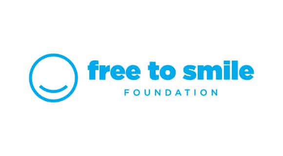 Blue logo with a smiling face and text reading "Free to Smile Foundation." Minimalistic design, focused on spreading positivity and support.