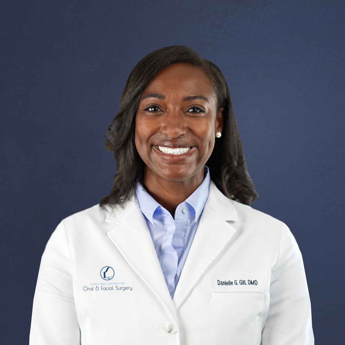 A smiling person in a white coat stands against a navy background, "Carolinas Center for Oral & Facial Surgery" visible on the garment.