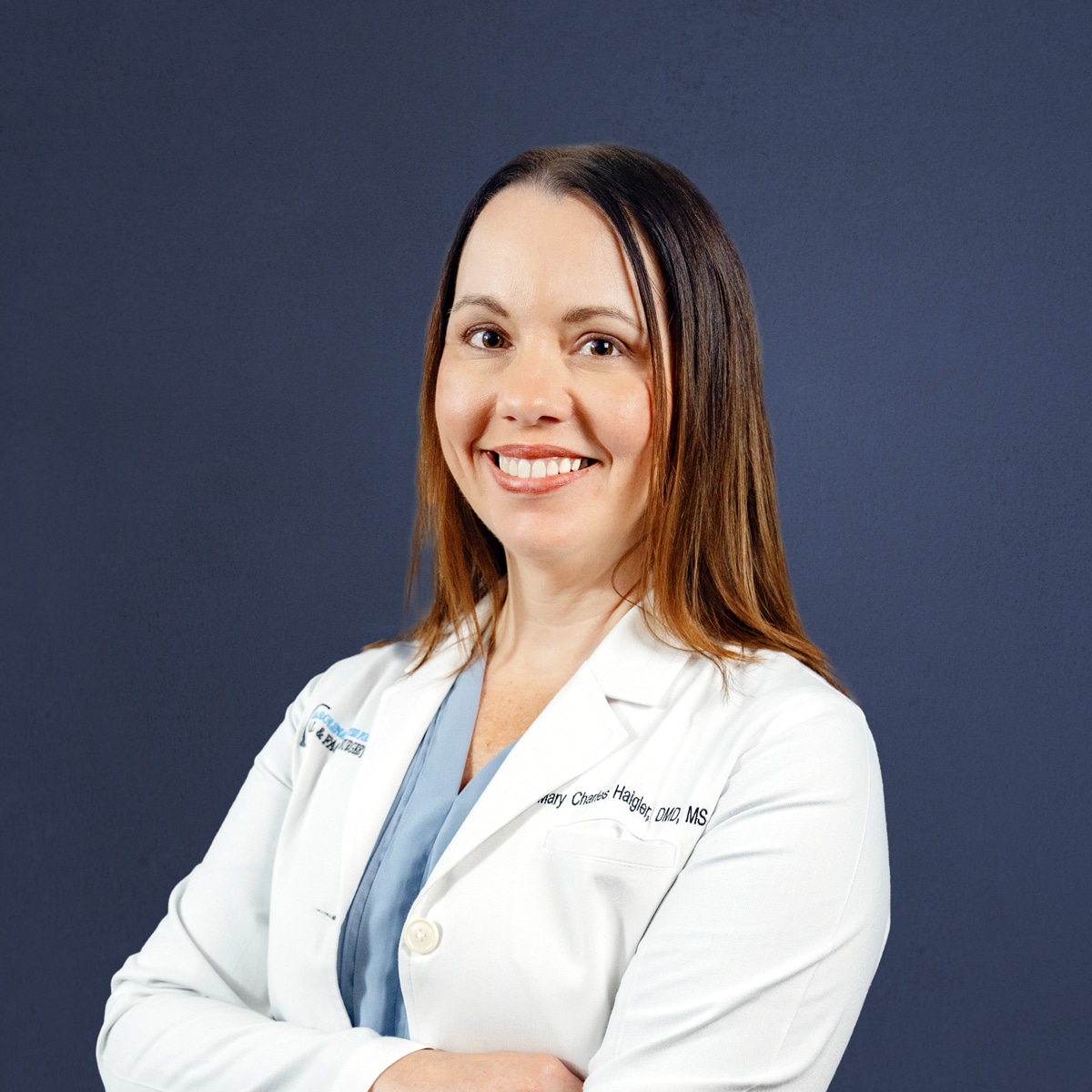 A person in a white lab coat smiles confidently at the camera against a solid dark background.