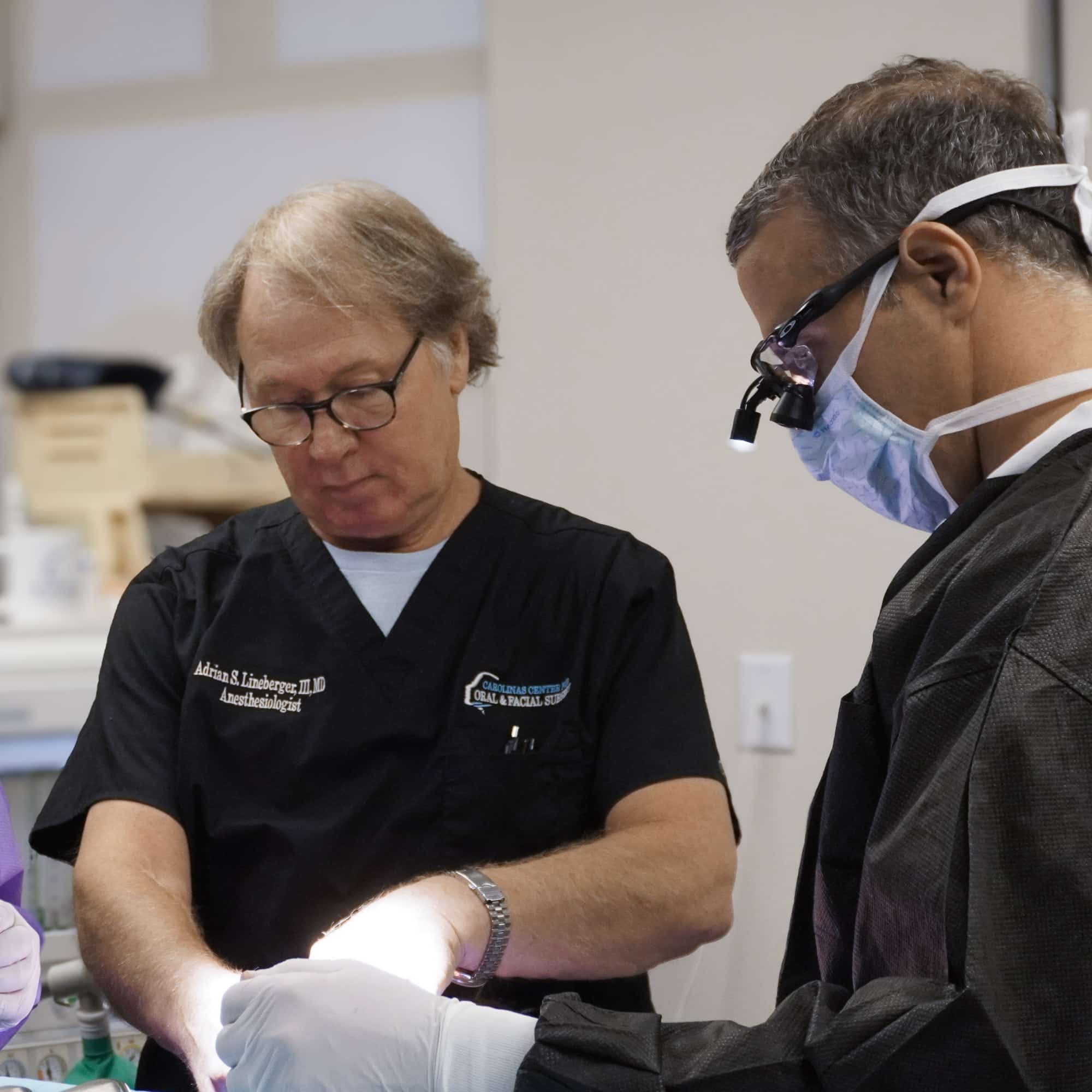 Two medical professionals in scrubs focus on a surgical procedure, using specialized equipment, in a clinical setting.