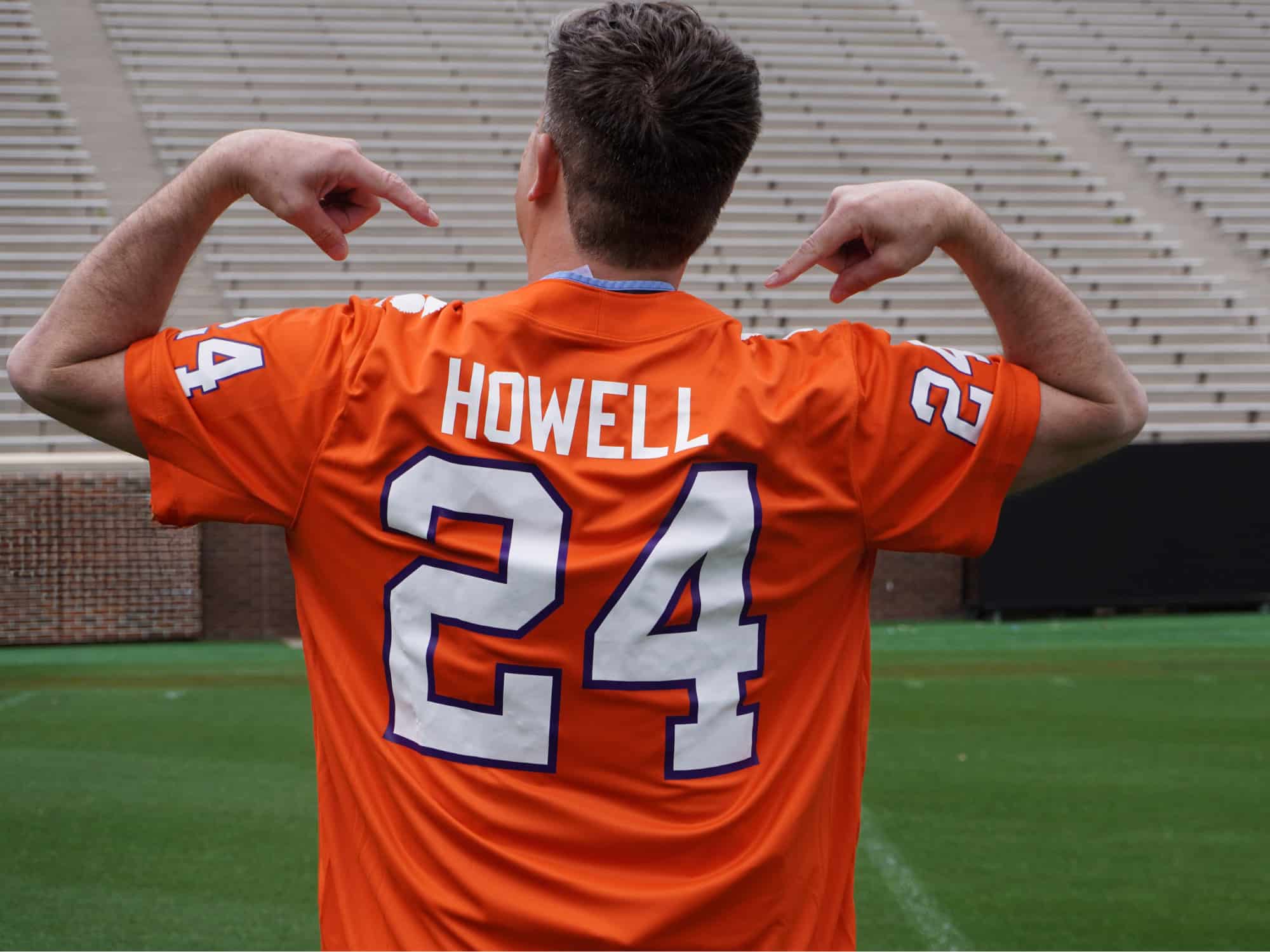 A person wearing an orange jersey, labeled "Howell 24," points at their name in an empty stadium, likely a sports venue.