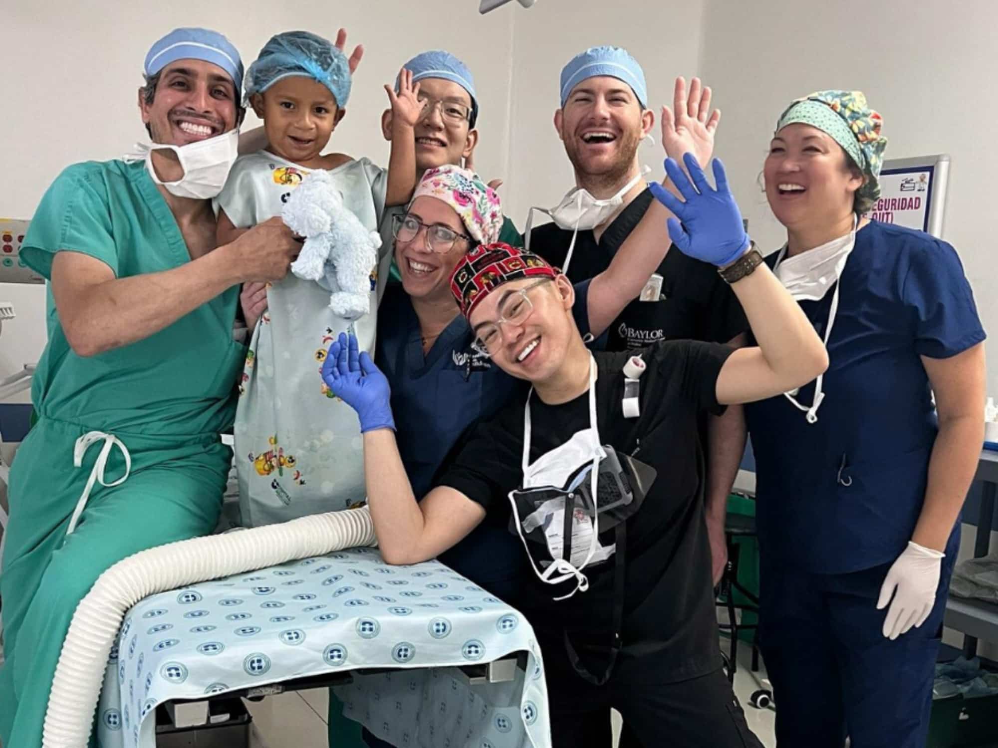 A joyful group of medical professionals and a child, wearing surgical attire, pose cheerfully in a hospital setting.