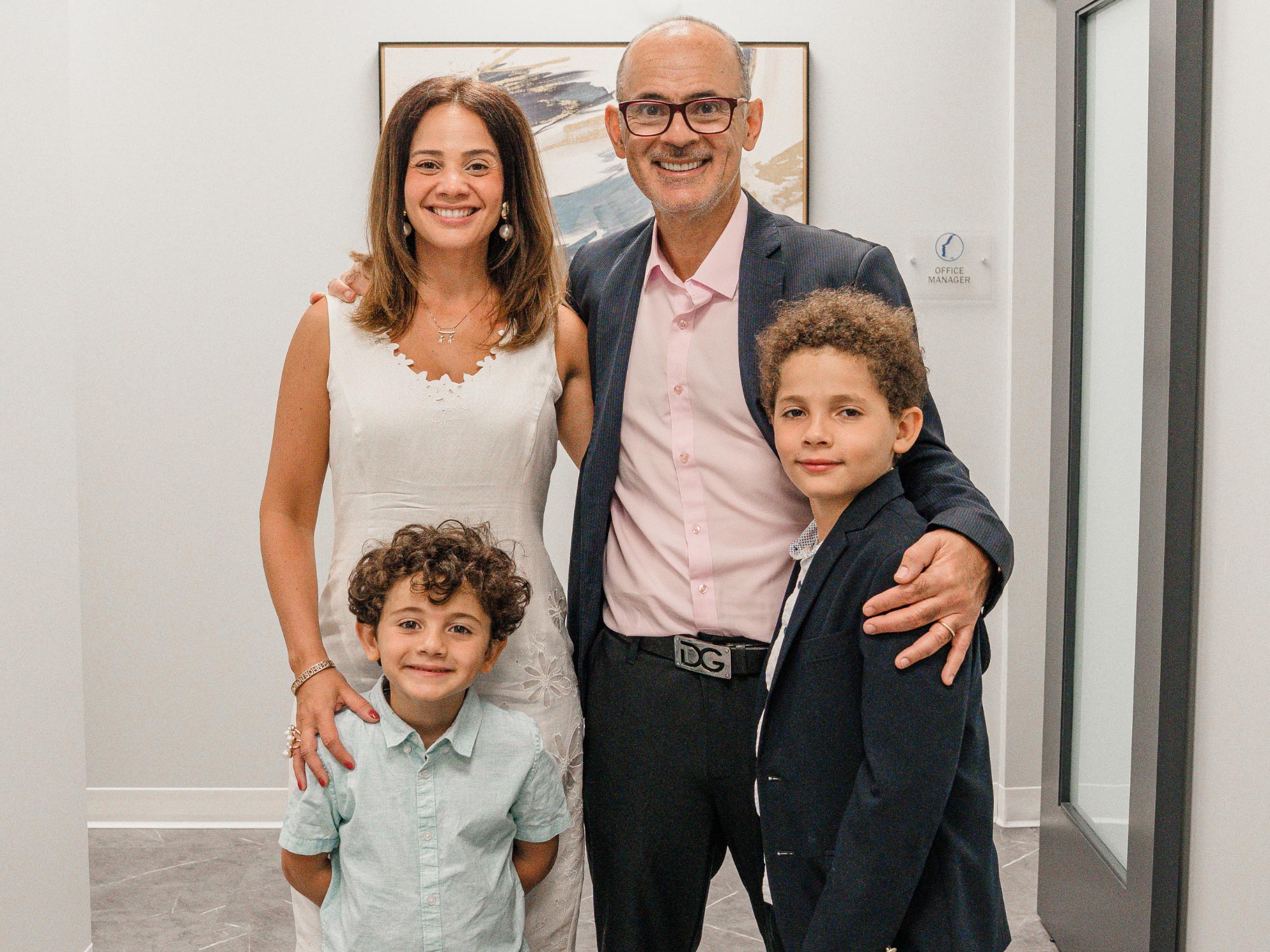 A smiling group of four, two adults and two children, are in a modern indoor setting with abstract art on the wall.