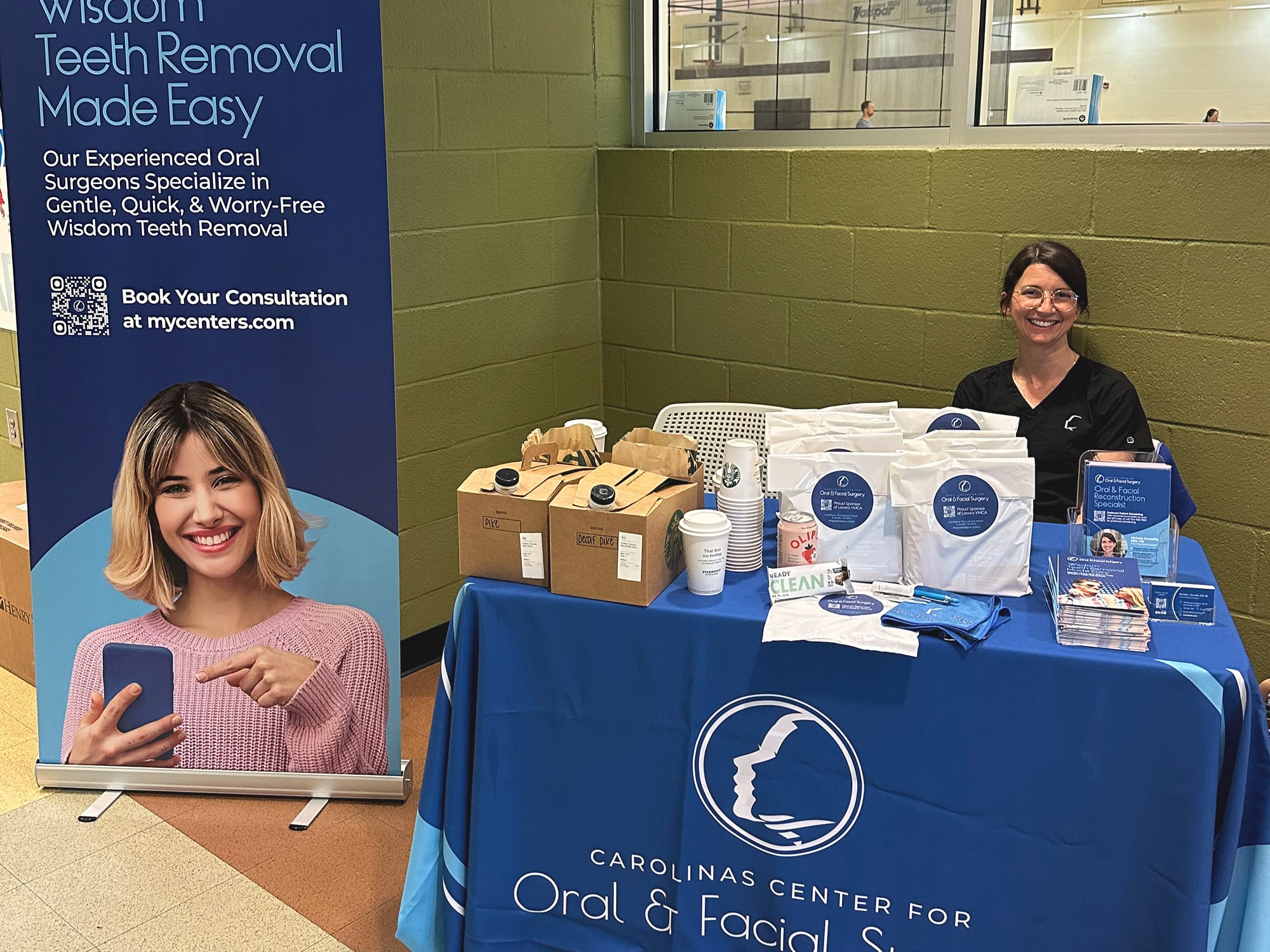 A person at a dental surgery information booth with promotional materials and a large poster showcasing wisdom teeth removal services.