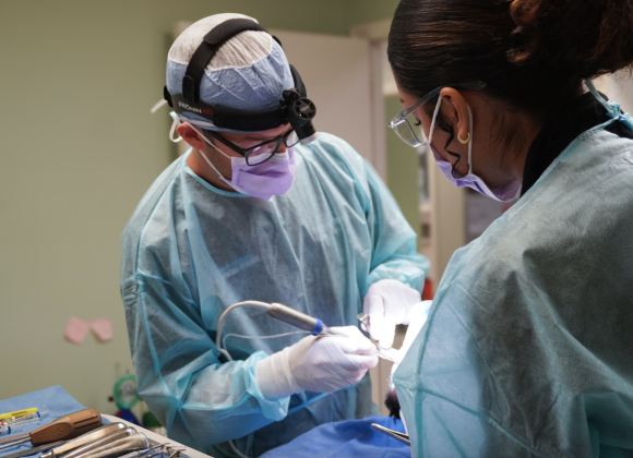 An oral surgeon and surgical assistant performing a wisdom teeth extraction procedure.